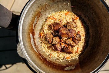 real Uzbek pilaf in a cauldron. Carrots and meat in a cauldron with rice on a live fire in a huge cauldron for pilaf
