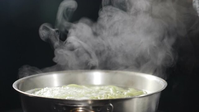 Italian cuisine. pasta being cooked in boiling water. White smoke in slow motion rising above hot saucepan on black background. Cooking in restaurant. Delicious Italian pasta. Full hd