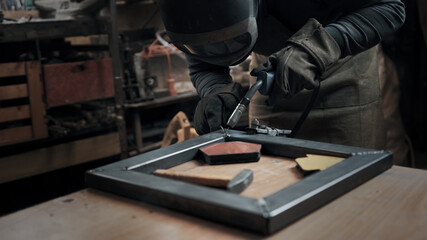 Worker wearing a mask and gloves soldering metal parts