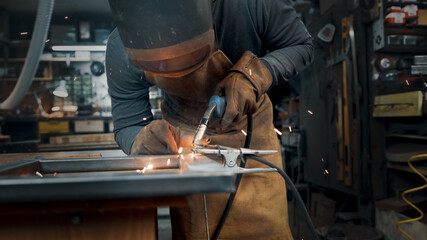 Worker wearing a mask and gloves soldering metal parts