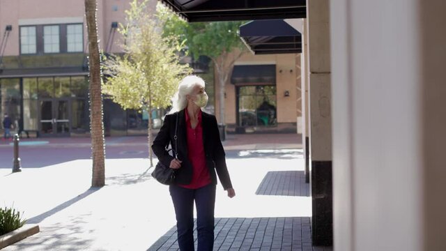 Wearing a mask in compliance with COVID19 mandates a mature woman doing a little outside window shopping at town center.
