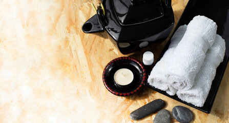  Black ceramic teapot in oriental style aroma lamp and aroma oil rolls of white towels on a ceramic dish and sea pebbles for face massage. Border for spa theme health and face and body care.