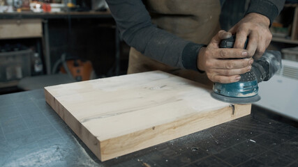 A carpenter grinds a piece of wood for a loft-style chair. Close up.