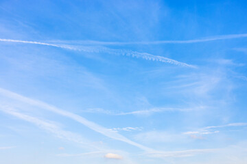 several old contrails and cirrus clouds in blue sky on autumn day