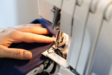 tailor overcasting the edge of fabric on household overlocker close up at home