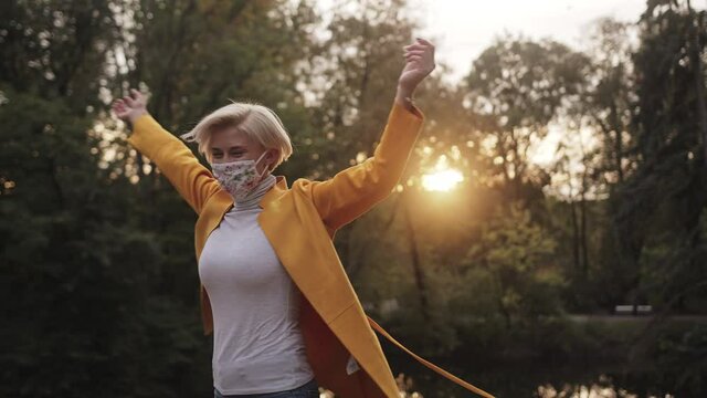 Young fashionable happy blond woman spinning in the nature with face mask