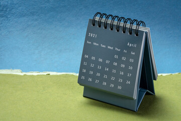 April 2021 - spiral desktop calendar against paper landscape abstract, time and business concept