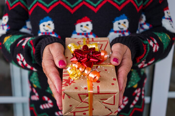 Female hands holding a christmas present. Background of a winter sweater