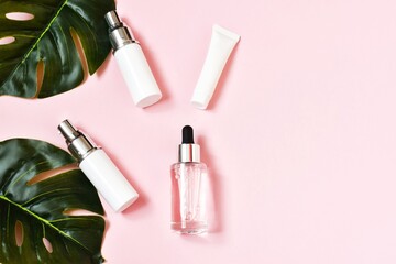 Natural skincare cosmetic bottles with monstera leafs on a pink background. Bio beauty products packaging design. Flat lay, top view. Copy space.