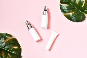 Natural skincare cosmetic bottles with monstera leafs on a pink background. Bio beauty products packaging design. Flat lay, top view. Copy space.