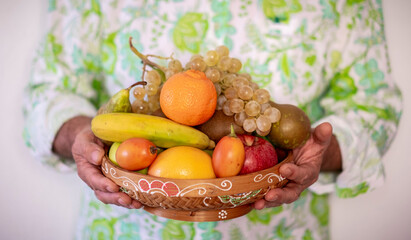 Hands of a man holding a brown bowl full of fresh healthy fruit. Concept of healthy eating and diet