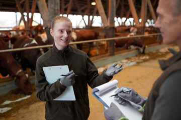 High angle view at two workers talking while standing in livestock shed at family farm, copy space