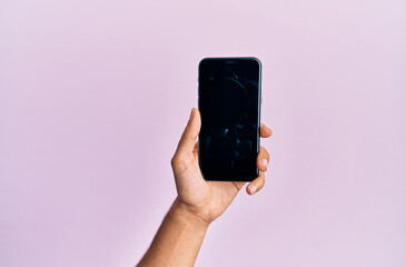 Hand of young hispanic man showing smartphone over isolated pink background.