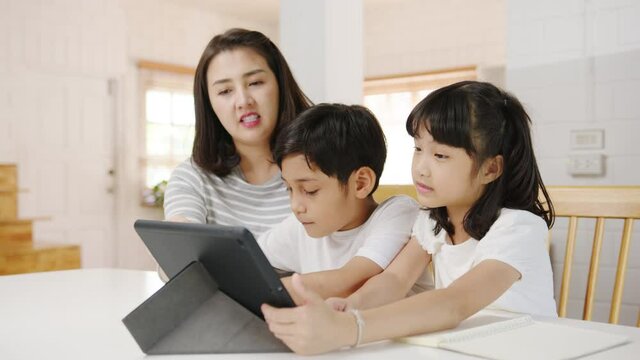 Happy Asia family homeschooling, mother teach children using digital tablet in living room at home. Spending time together, Self-isolation, Social distancing, Quarantine for corona virus prevention.