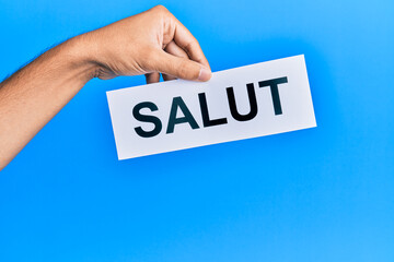 Hand of hispanic man holding salut word paper over isolated blue background.