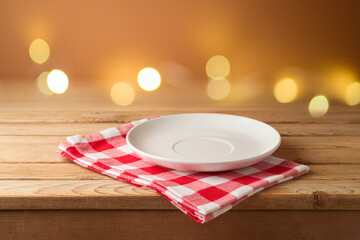Empty plate with checked tablecloth on wooden table over festive lights bokeh background