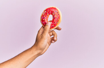 Hand of hispanic man holding donut over isolated pink background.