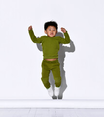 Faceless dark-haired little boy jumps on the background of a white wall in the studio.