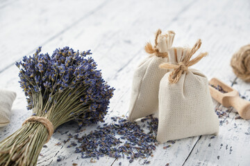 Dry lavender flower bouquets and aromatic sachets on white wooden table.