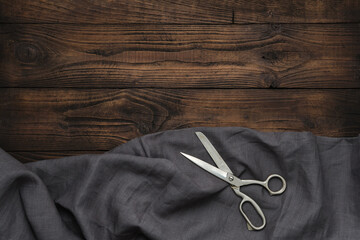 Tailoring scissors and gray linen cloth on wooden background. Copy space for text.