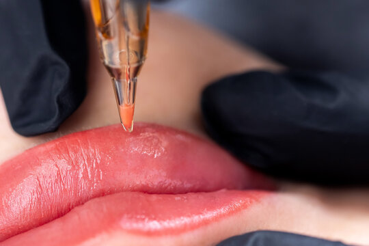 Macro photo of process of applying permanent makeup tattoo of red on lips woman