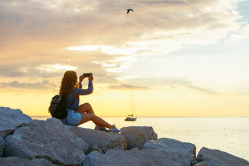 woman with backpack looking on sunset over the sea