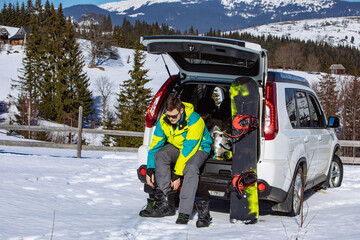 man sitting in car trunk changing for snowboard