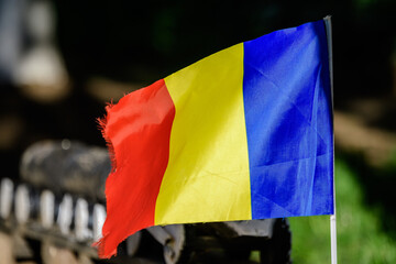 Romanian national flag blowing in the wind in direct sunlight towards blurred background.