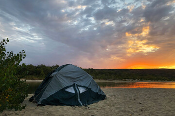 breathtaking view of colorful sunset on river, touristic tent is on river shore., in beautiful place. Adventure concept.