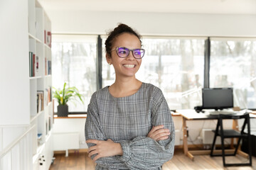 Happy sincere young african american female employee businesswoman in eyeglasses standing in modern...