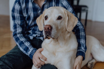 Lifestyle Portrait von jungem Mann mit seinem Labrador Retriever beim Kuscheln im Wohnzimmer