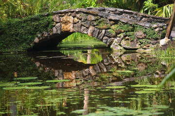Fototapeta na wymiar Old stone arch over a pond reflecting in the water