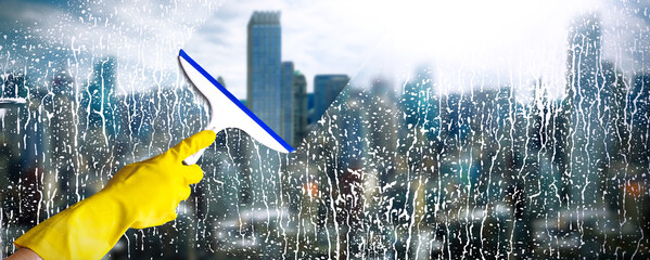 Cleaning windows with skyscraper on background. Hand in yellow glove hold cleaning squeegee. Cleaning service concept.