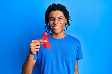 Young african american man holding support red ribbon looking positive and happy standing and...