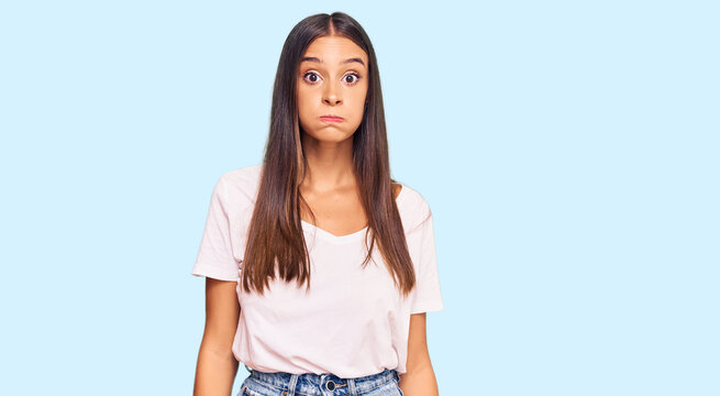Young hispanic woman wearing casual white tshirt puffing cheeks with funny face. mouth inflated with air, crazy expression.