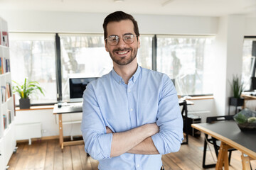 Portrait of happy handsome 30s businessman in eyeglasses standing in modern creative workplace with...