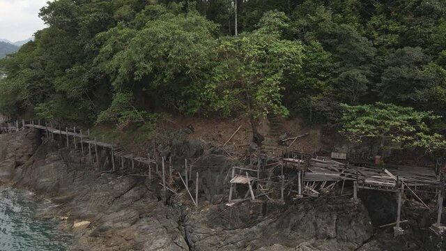 Drone left trucking orbit shot , birds eye view of a broken down wooden walkway along a granite rock coastline on a tropical Island with jungle lush green forest and ocean