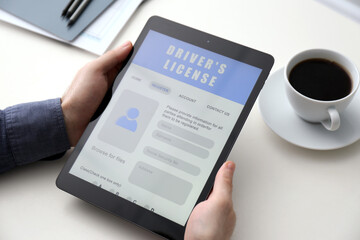 Man holding tablet with driver's license application form at white table, closeup