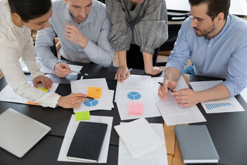 Top view focused young serious multiracial teammates involved in analyzing marketing research...
