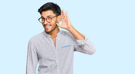 Young handsome man wearing casual clothes and glasses smiling with hand over ear listening an hearing to rumor or gossip. deafness concept.