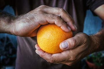 two male hands are holding an orange