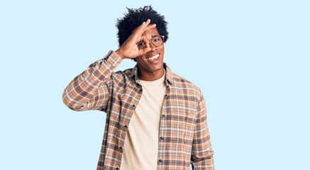 Handsome african american man with afro hair wearing casual clothes and glasses doing ok gesture with hand smiling, eye looking through fingers with happy face.