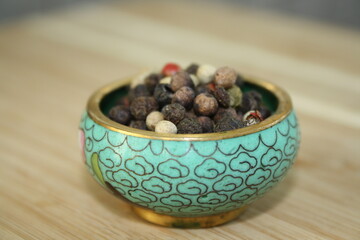 peppercorns in a ceramic plate on a wooden background