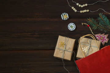 Christmas shopping. Gift red paper bag with kraft paper boxes with golden snowflakes on dark wooden background. Wooden beads with the inscription Happy New Year. Copy space. Festive concept.