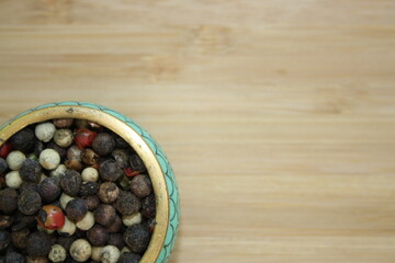 peppercorns in a ceramic plate on a wooden background