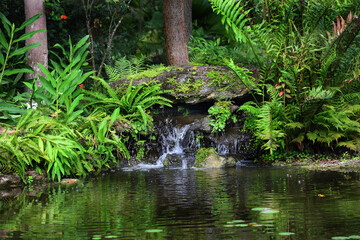 Natural rock waterfall surrounded by red flowers and green foliage