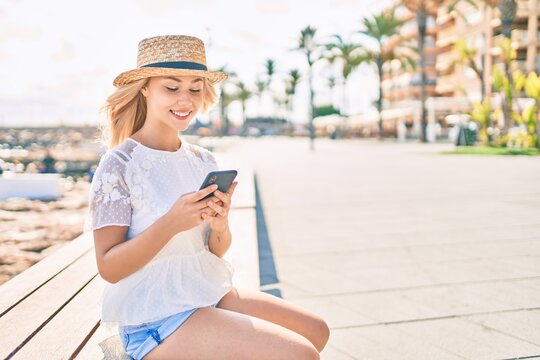 Young caucasian tourist girl smiling happy using smartphone sitting on bench at promenade.