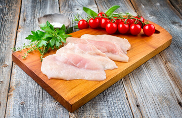 Raw traditional chicken escalope with tomatoes and herbs offered as close-up on a modern design...
