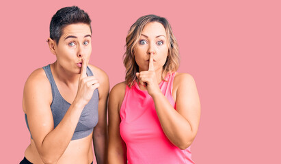 Couple of women wearing sportswear asking to be quiet with finger on lips. silence and secret concept.