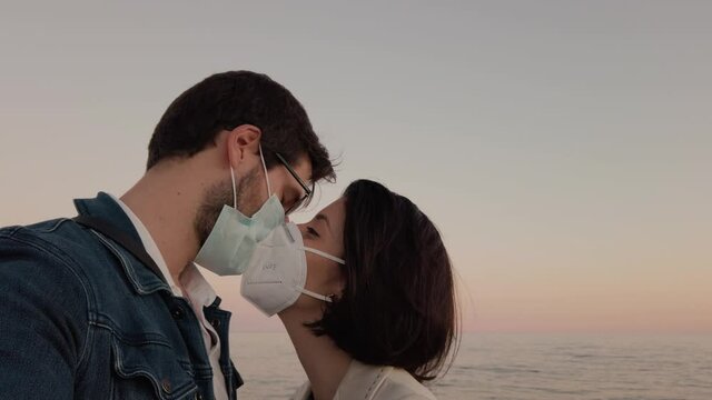 Ragazzo e ragazza si baciano con la mascherina in spiaggia di fronte al mare nel giorno di San Valentino